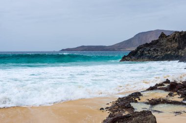 Playa de las Conchas sahilinde kayalara çarpan dalgalar
