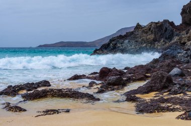 Playa de las Conchas sahilinde kayalara çarpan dalgalar