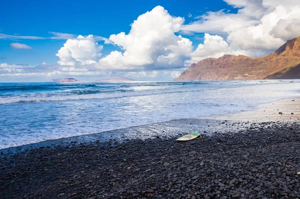 Bir sörf tahtası ile Famara Volkanik plaj bir dalga bekliyor — Stok fotoğraf