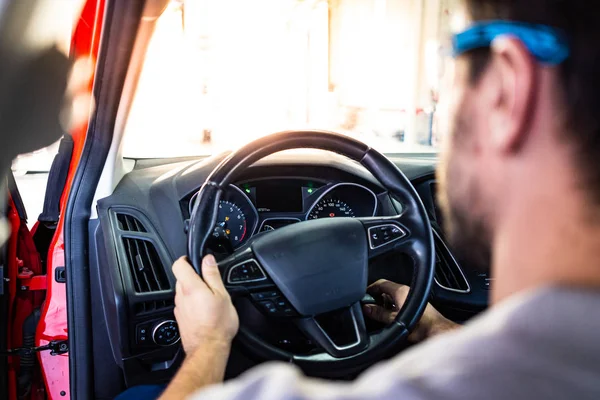 Bir araç muayenesi sırasında bir arabanın motorını çalıştıran güvenlik gözlüklü teknisyen