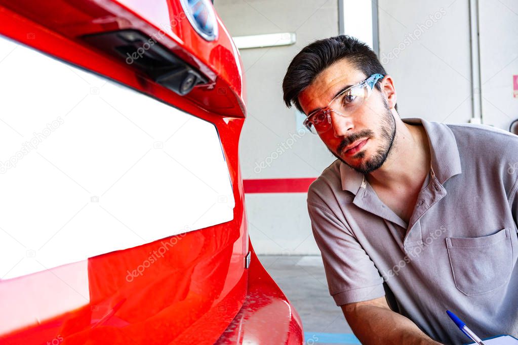 Technician with safety glasses inspecting the rear view camera of a car in a vehicle inspection workshop