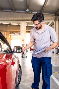 Bir araç muayene atölyesinde bir arabanın sağ dikiz teftiş güvenlik gözlükleri ile Teknisyen