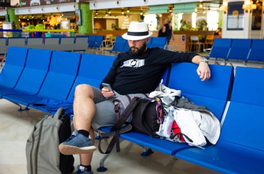 Havaalanında bavuluyla bekleyen şapkalı genç adam