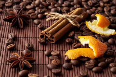 Kavrulmuş kahverengi kahve çekirdekleri, tarçın çubukları, anason ve portakal tadı koyu bir arka planda.