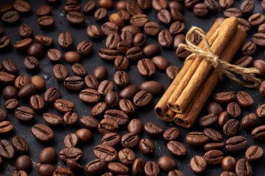 Kahverengi kahve çekirdekleri kavrulmuş ve koyu bir arka planda tarçın çubukları bağlanmış.