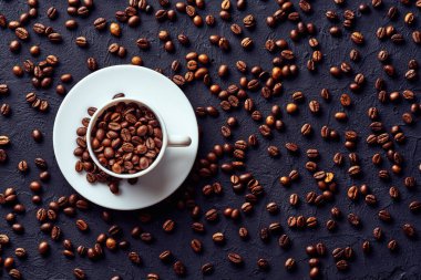 Kahverengi kahve çekirdeklerinin üst görüntüsü beyaz porselen bardakta gri desenli arka planda çay tabağında.