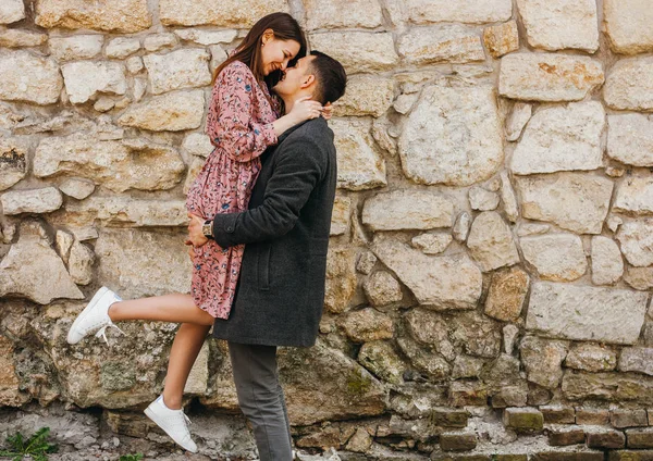 Happy young man holding his woman in his arms against stone background. — Stock Photo, Image