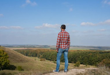 Bir tepede duran genç adam manzaranın tadını çıkarıyor. Seyahat ve özgürlük kavramı.