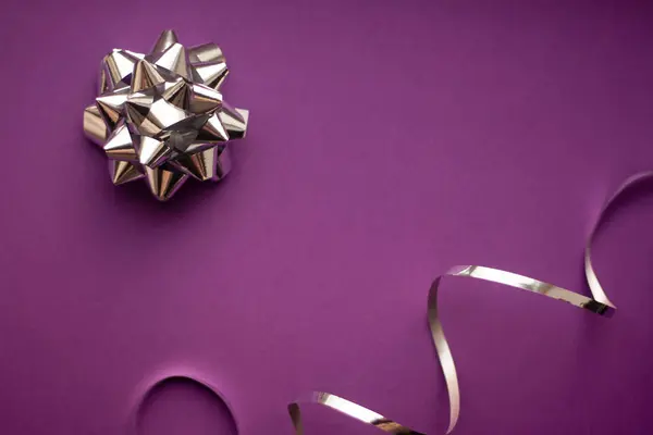 Silver ribbon and bow against pink background. Minimal style.