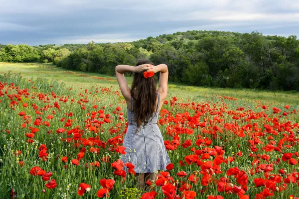 Молодая женщина стоит в ярком поле красных маков. Драматическое облачное небо . — стоковое фото