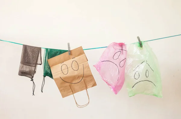 Plastic bags with sad emotions and paper and eco bags with happy emotion against white background. Ecology concept.
