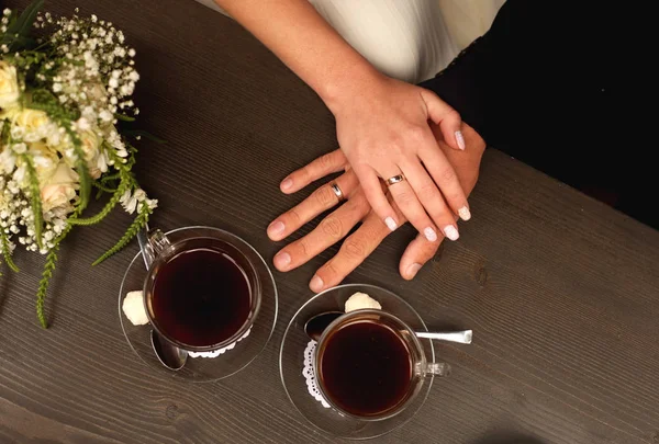 Bräutigam und Braut Hände mit Ringen auf dem Tisch mit zwei Kaffeetassen, Nahaufnahme von oben — Stockfoto