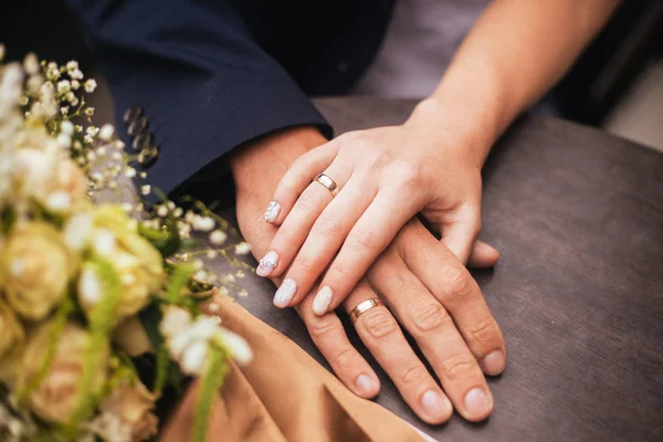 Nahaufnahme eines frisch verheirateten Paares, das sich mit Ringen und einem Blumenstrauß an den Händen hält. — Stockfoto