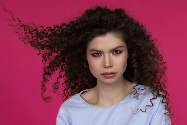 Young beautiful Caucasian with afro curls hairstyle wearing blue blouse on magenta background