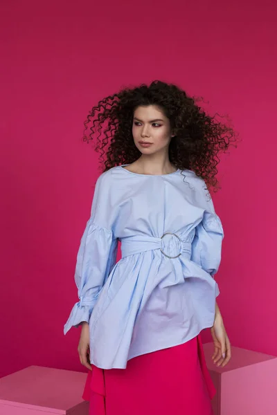 Young beautiful Caucasian with afro curls hairstyle wearing blue blouse on magenta background