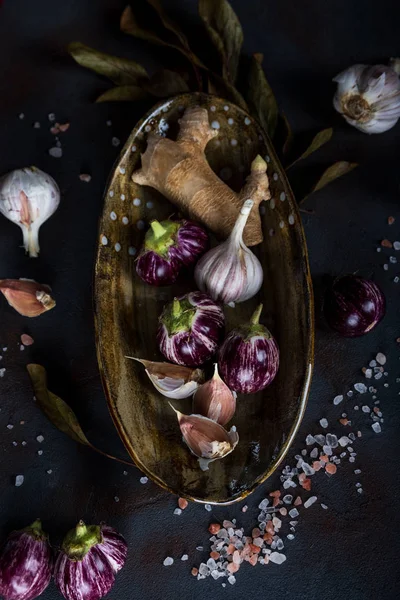 Mini Eggplants, ginger, garlic in handmade ceramic plate, crystalline pink salt on concrete background