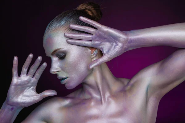 Beautiful female model with pearl shining colourful body art on face and body. Headshot of model poses with hands next to face.