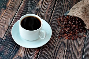  Tahta bir masanın üzerinde dağınık taneli beyaz bir fincan kahve.