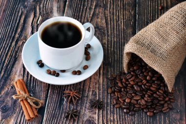 Tarçın, anason ve dağınık kahve çekirdeklerinin yanında, ahşap bir masanın üzerinde beyaz bir fincan kahve.