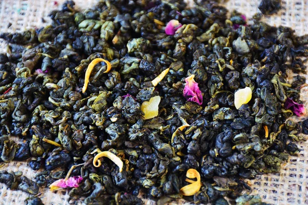 Dried green tea with fruit slices and flower petals on burlap.