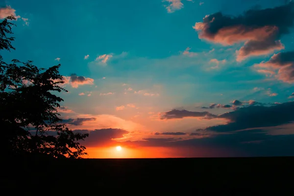 Sunset sunrise over field or meadow. Bright dramatic sky and dark ground. Countryside landscape under scenic colorful sky at sunset dawn sunrise.