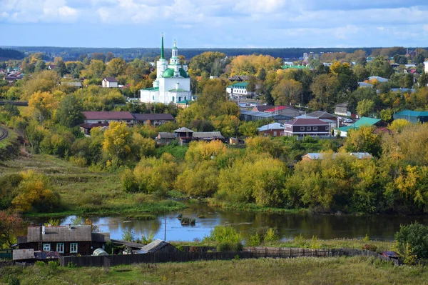 Alapayevsk スヴェルドロフスク州 ロシア 2020年9月12日 ホーリートリニティ大聖堂 川とフォアグラウンドで居心地の良い木造の家とアラパエスクのパノラマ 緑の絵の町 ストック画像