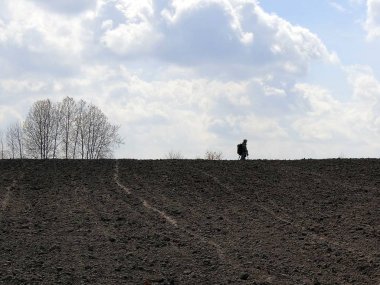 Bir adam ile bir metal detektörü sürülmüş bir alanında, bir arka plan gökyüzü ve bulutlar
