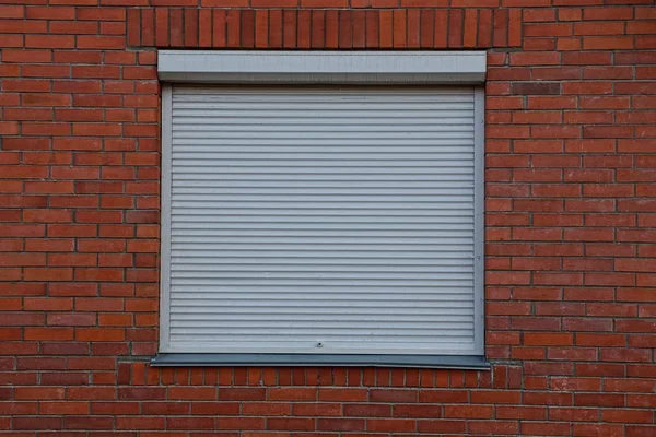 The square window closed by gray jalousie on a brick wall