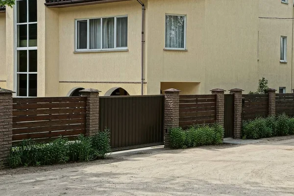 brown wooden fence and gate in the grass near the road near a large house with windows