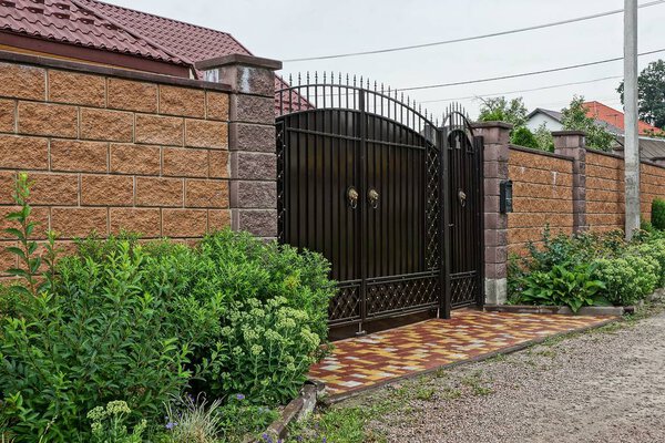 large brown gate and brick fence in green decorative grass on the street