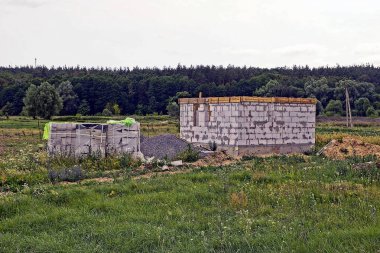 Çimlerin üzerinde bitmemiş beyaz tuğlalı bir ev olan inşaat alanı.