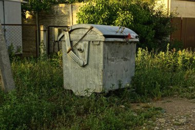 bir gri metal kapalı çöp kutusu yeşil çim tarafından yolda duruyor