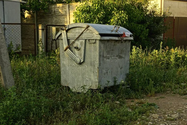 bir gri metal kapalı çöp kutusu yeşil çim tarafından yolda duruyor