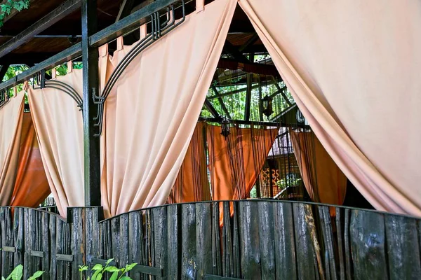 Part of the restaurant with beautiful curtains behind a brown fence