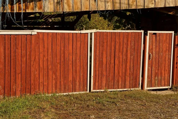 red wooden fence with gate and wicket outside in the grass
