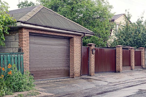Brown gate in a private garage and an iron gate with a mailbox near the road