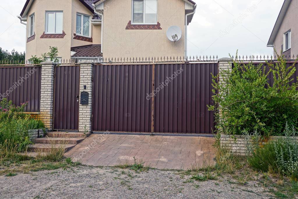 fence and brown gate of metal overgrown with green plants in front of a private house