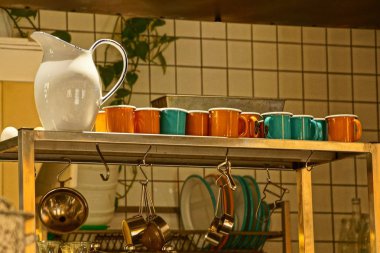 bir büyük beyaz sürahi ve bir satır renkli kupalar ve bardaklar mutfakta rafta