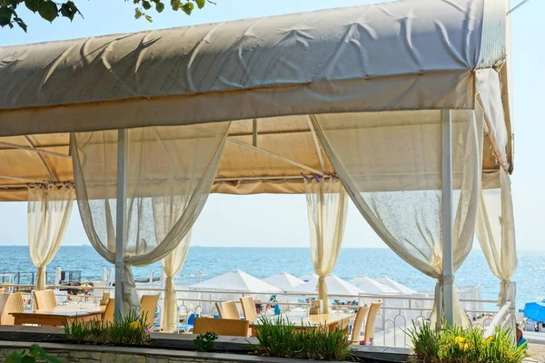 part of the white veranda of the restaurant with curtains and furniture on the background of the sea