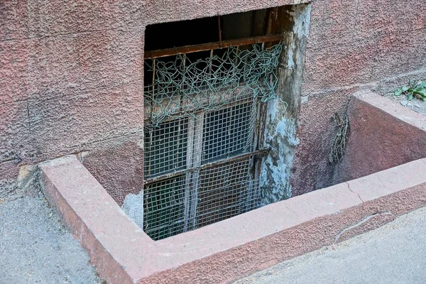The old window behind the bars in the basement on the wall by the sidewalk