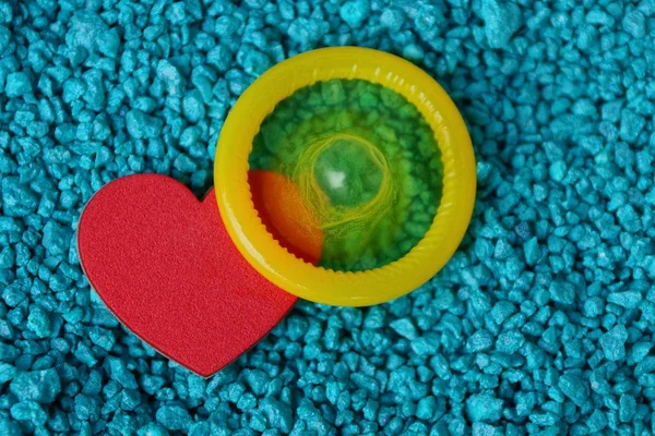 红色心脏和黄色避孕套在蓝色石渣 — 图库照片