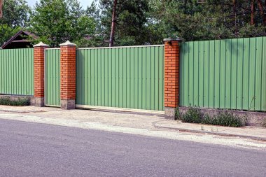 Yeşil çit ve kapıları önünde asfalt yol