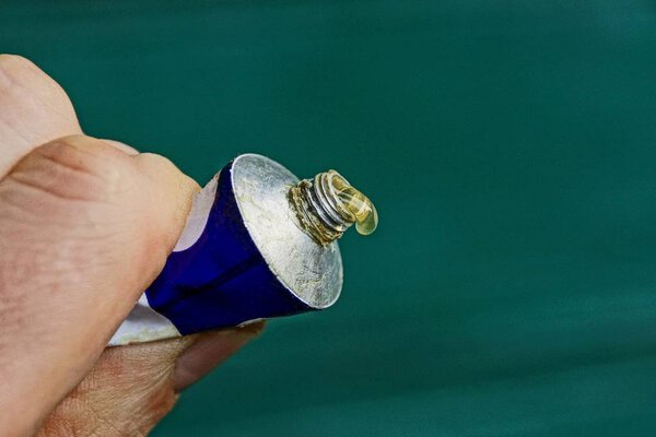 Drop of glue on a tube squeezed in a hand