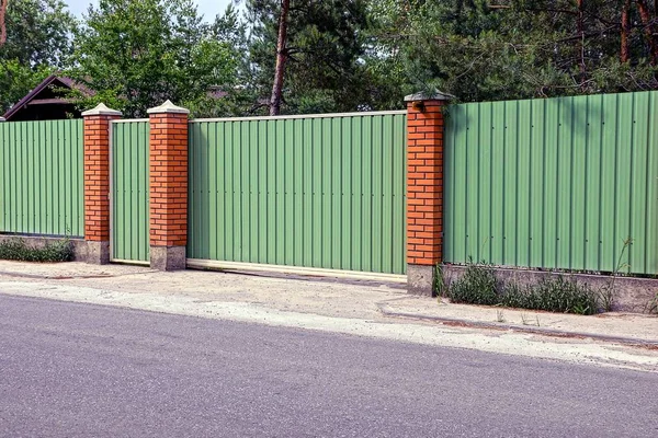 Green fence and gates in front of the asphalt road