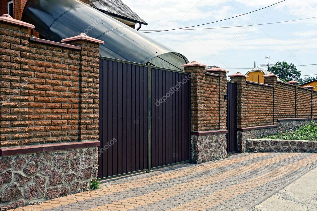 Brown brick fence and iron gates in front of the house