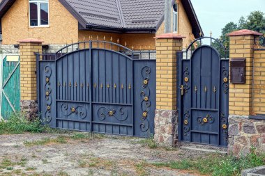 Siyah metal kapılar ve kapılar. Sahte desenli ve tuğla bir çitin parçası.