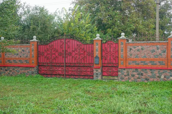 private red iron gate with a wrought iron pattern with a stone fence in the street