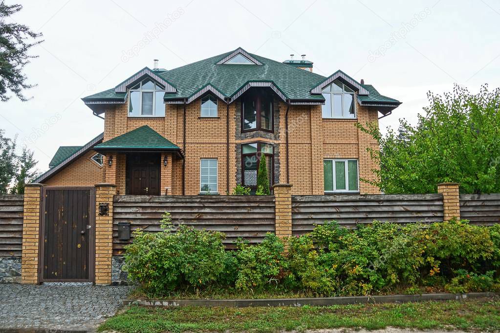 private brown brick house with windows behind a wooden fence in the grass