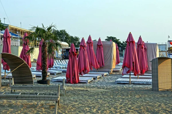 a lot of red umbrellas and brown sun beds in the sand on the morning beach