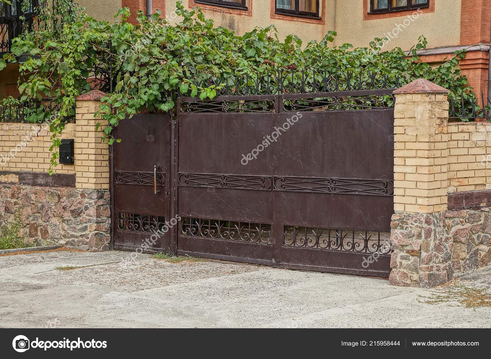 Old Brown Iron Gate Brick Fence Green Vegetation Street Stock Photo by